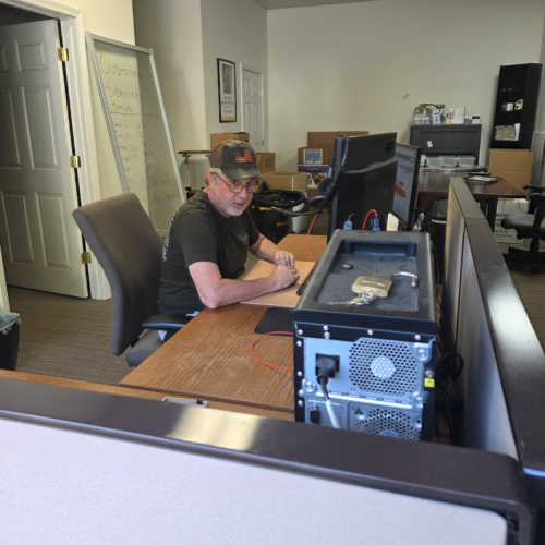 Chris is sitting at a desk wearing glasses and a baseball cap