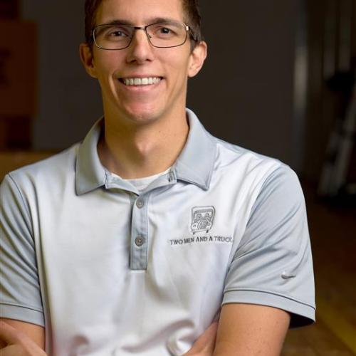 Dylan is smiling with arms crossed, wearing a grey two men and a truck polo shirt. 