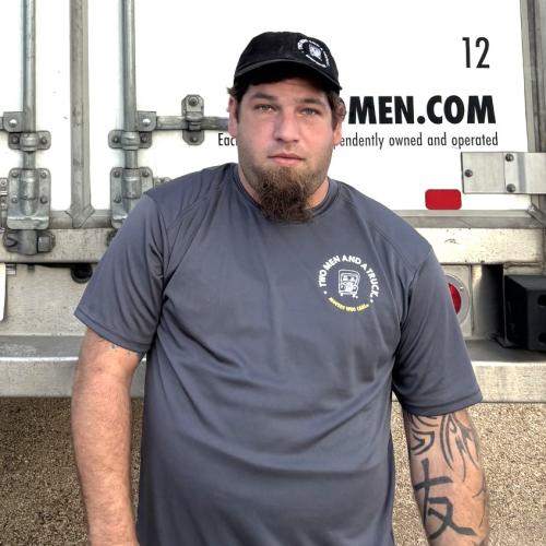 Chris is standing in front of a two men and a truck moving van wearing a two men and a truck tshirt and cap