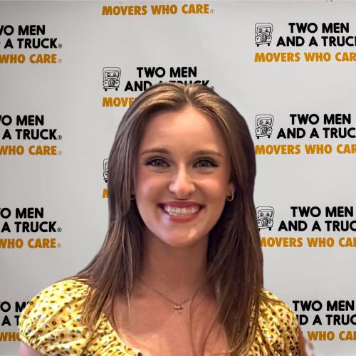 kassidie standing in front of two men and a truck logo background wearing yellow floral top