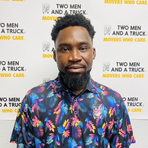 Samuel wearing multicolored floral polo standing in front of two men and a truck backdrop