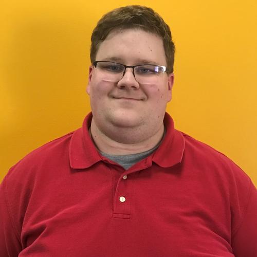 Josh wearing a red polo, smiling, standing in front of a yellow wall