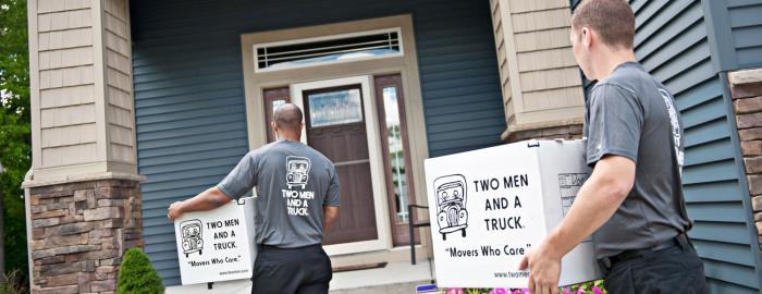 two men and a truck movers carrying boxes into a house