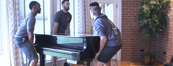 Two Men And A Truck movers lifting a piano